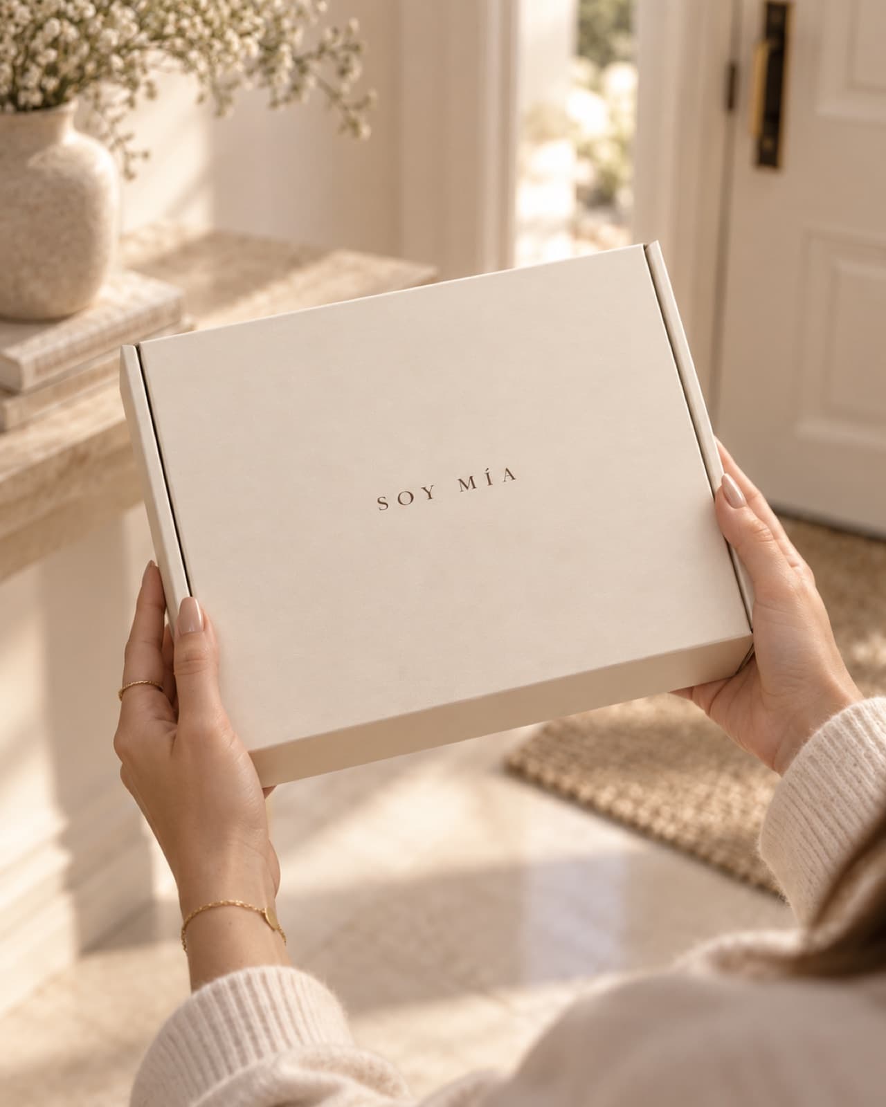 Unas manos sostienen una caja de regalo marfil al recibirla en casa